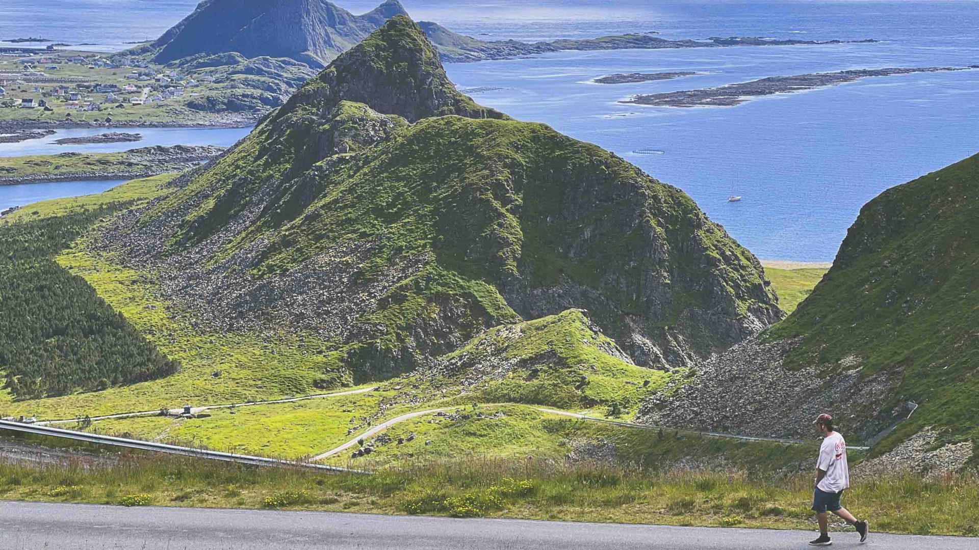 A person walks a path past green hills and blue water.